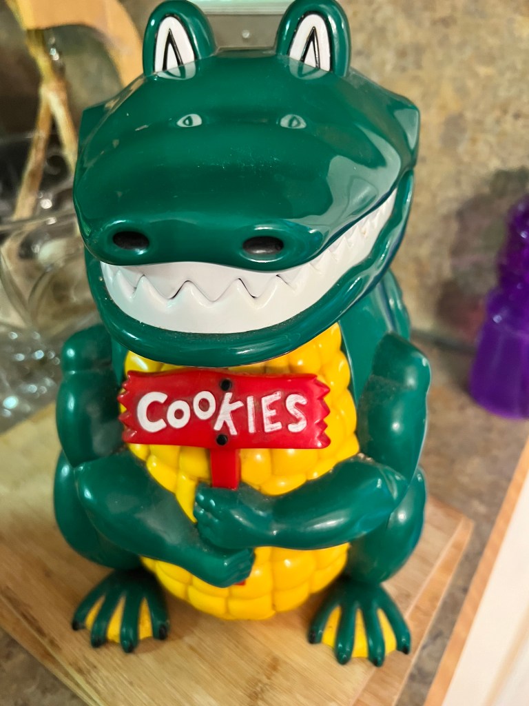Green alligator cookie jar holding a red sign that says Cookies
